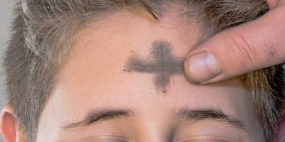 a person's forehead is marked with a cross using ash