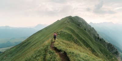 a young woman hikes along a grassy ridge in the Swiss Alps
