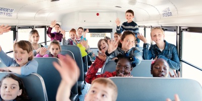 kids smiling and waving on a school bus