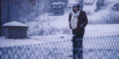 a girl walks along a chain-link fence during a winter blizzard