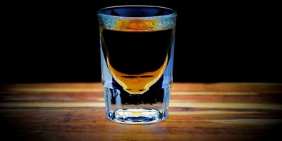 A shot glass filled with whisky and sitting on a bar