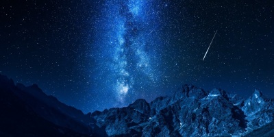 meteors falling over a rocky mountain range backed by the Milky Way
